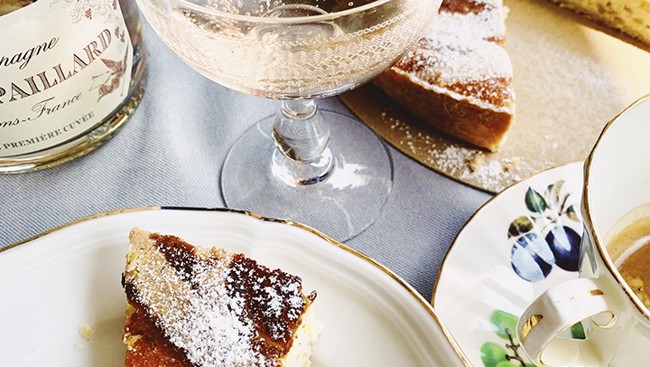 Een elegant ontbijt met taartpunt bestrooid met poedersuiker, een glas champagne en een kopje koffie op porseleinen servies.