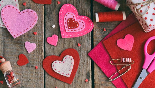 Gekleurde vilten hartjes, garen, schaar en veiligheidsspelden liggen op een houten tafel, klaar voor een knutselproject met valentijnthema.