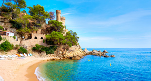 Zonnige kustlijn met turquoise zee, zandstrand, kleine boten en een groene klif met historische toren in Lloret de Mar.