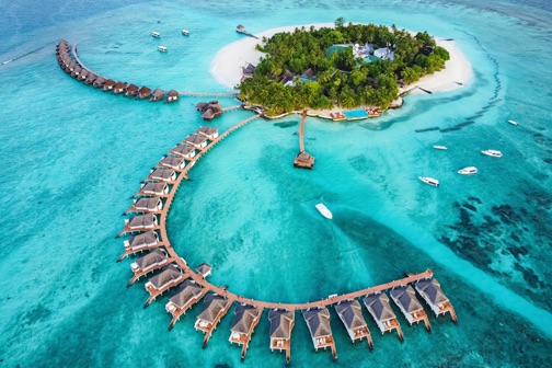 Luchtfoto van een tropisch eiland met wit zand en palmbomen, omringd door helder turquoise water en watervilla’s op palen in een ronde vorm.