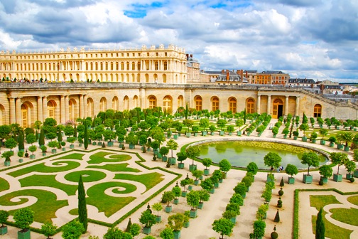Formele tuinen van het Paleis van Versailles met symmetrische parterres, vijvers en het paleis op de achtergrond onder een bewolkte lucht bij Parijs.