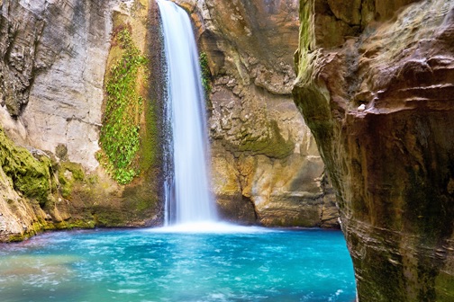 Hoge waterval die in een helderblauw bassin stroomt, omringd door steile rotswanden en groen mos in de Sapadere Canyon.