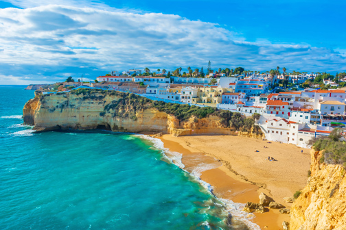 Zandstrand aan een heldere zee in de Algarve, omringd door hoge rotsen en witgekalkte huizen die trapsgewijs langs de kust zijn gebouwd.