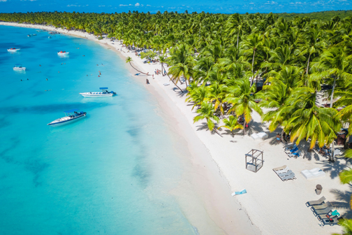 Bovenaanzicht van een tropisch wit strand op de Dominicaanse Republiek met veel palmbomen en boten in het blauwe water