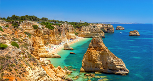 Gouden rotskliffen met natuurlijke bogen en grotten aan een turquoise kust, onder een heldere blauwe lucht in Albufeira