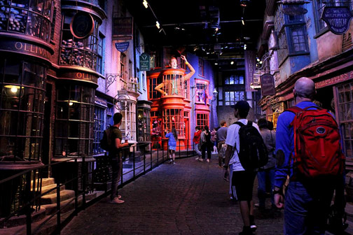 Donkere themastraat op filmset van Harry Potter Studio met kleurrijke winkelgevels vol borden en etalages, terwijl bezoekers over de kasseien lopen en om zich heen kijken.