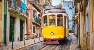 Trams rijden heuvels af in kleurrijke straat van Lissabon, Portugal met uitzicht op rivier.