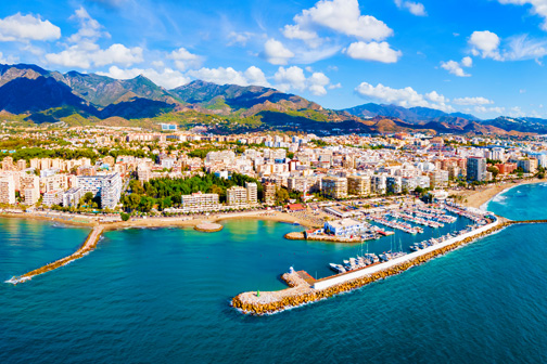 Luchtfoto van een kustplaats met jachthaven en pier, turquoise zee langs de stad en bergen op de achtergrond aan de Costa del Sol.